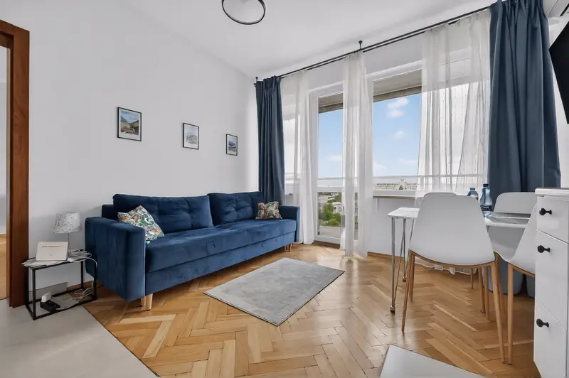 Salon z granatową kanapą, parkietem w jodełkę i oknami na miasto
